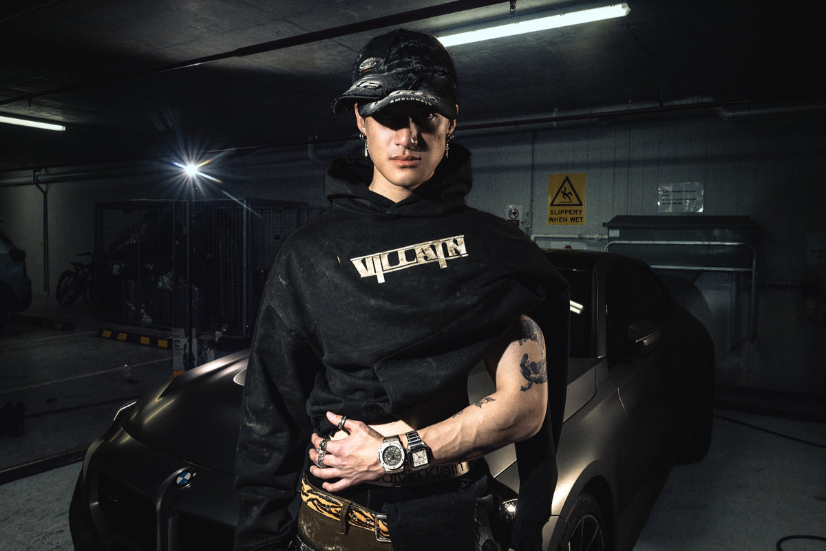 Model in a black Villain hoodie in front of a car
